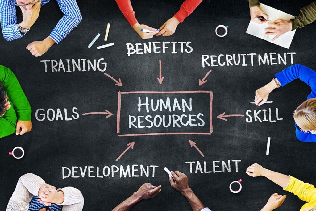 A diverse group of professionals write on a chalkboard, each person writing the various duties for human resources jobs.